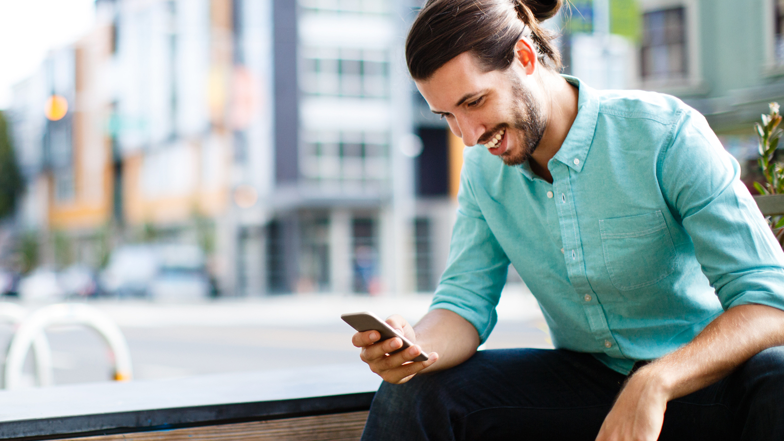 Seated man using smart phone in a city setting.